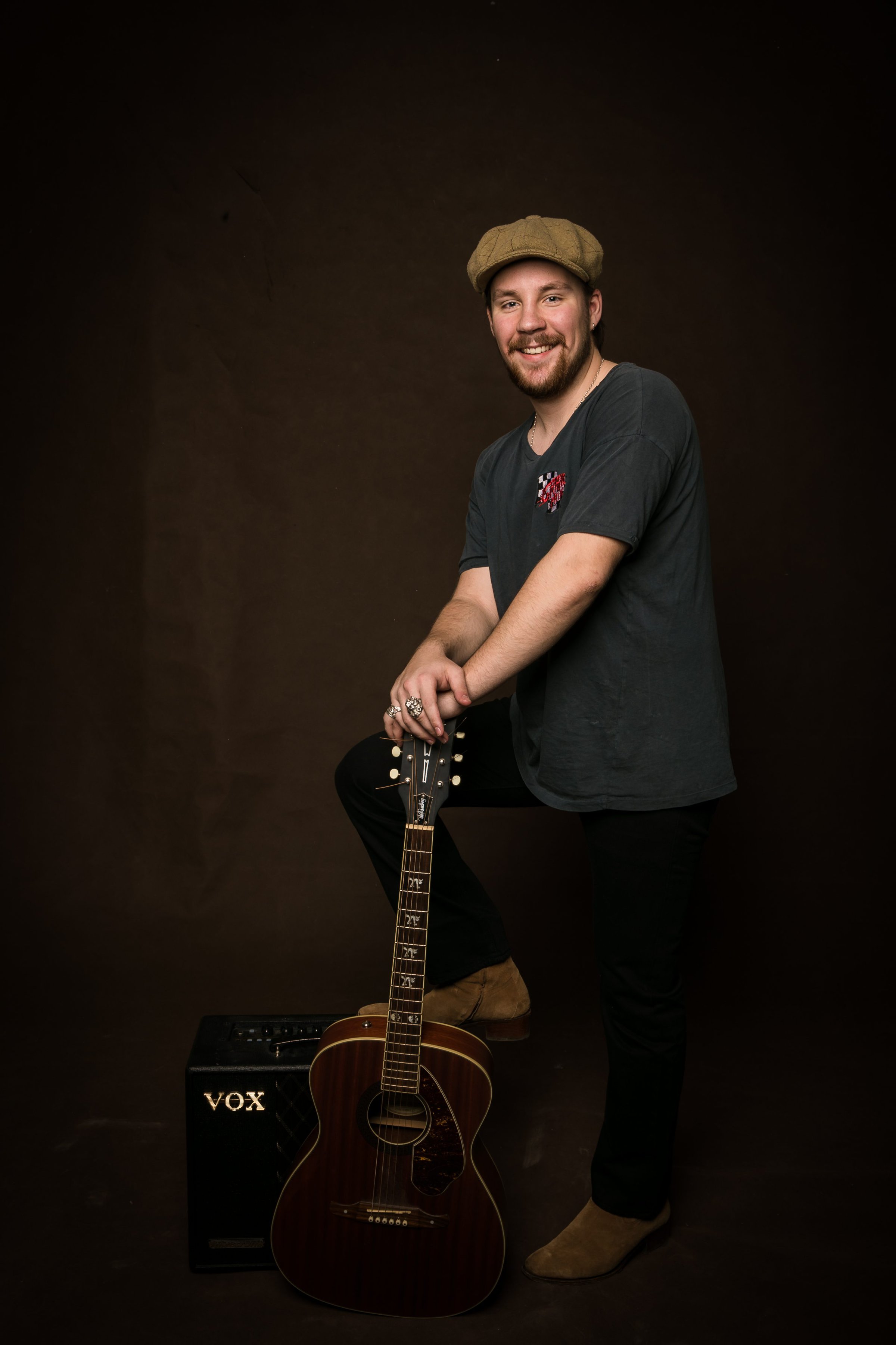 Cai Tonks stående med hat og sort baggrund