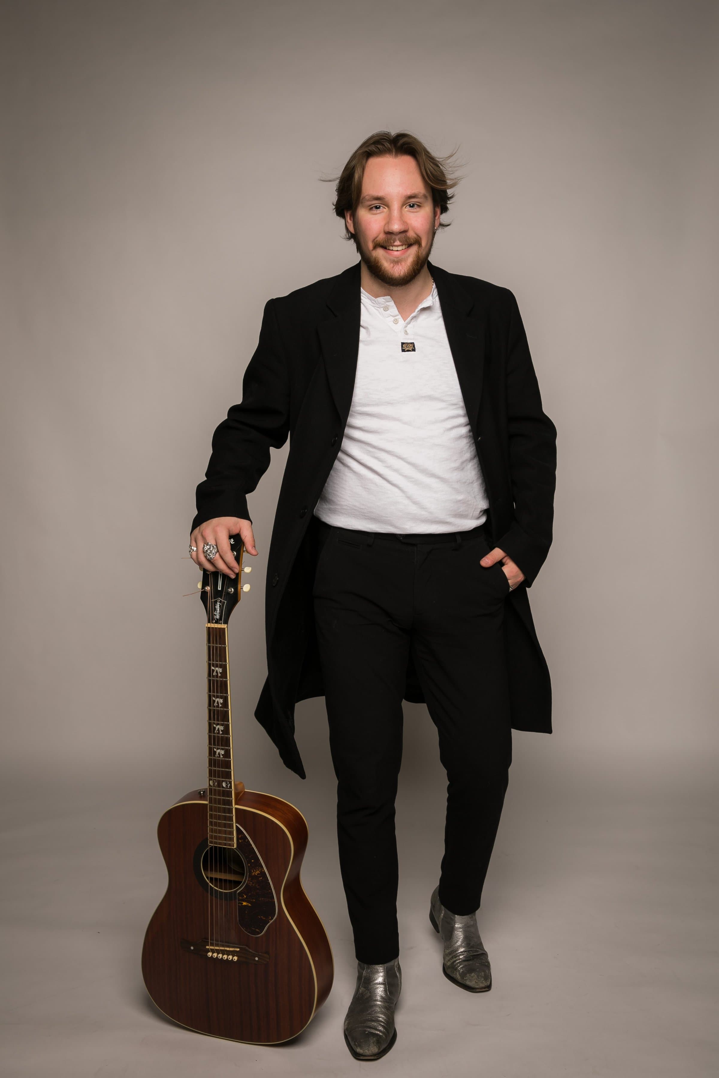 Cai Tonks stående og holder på guitar