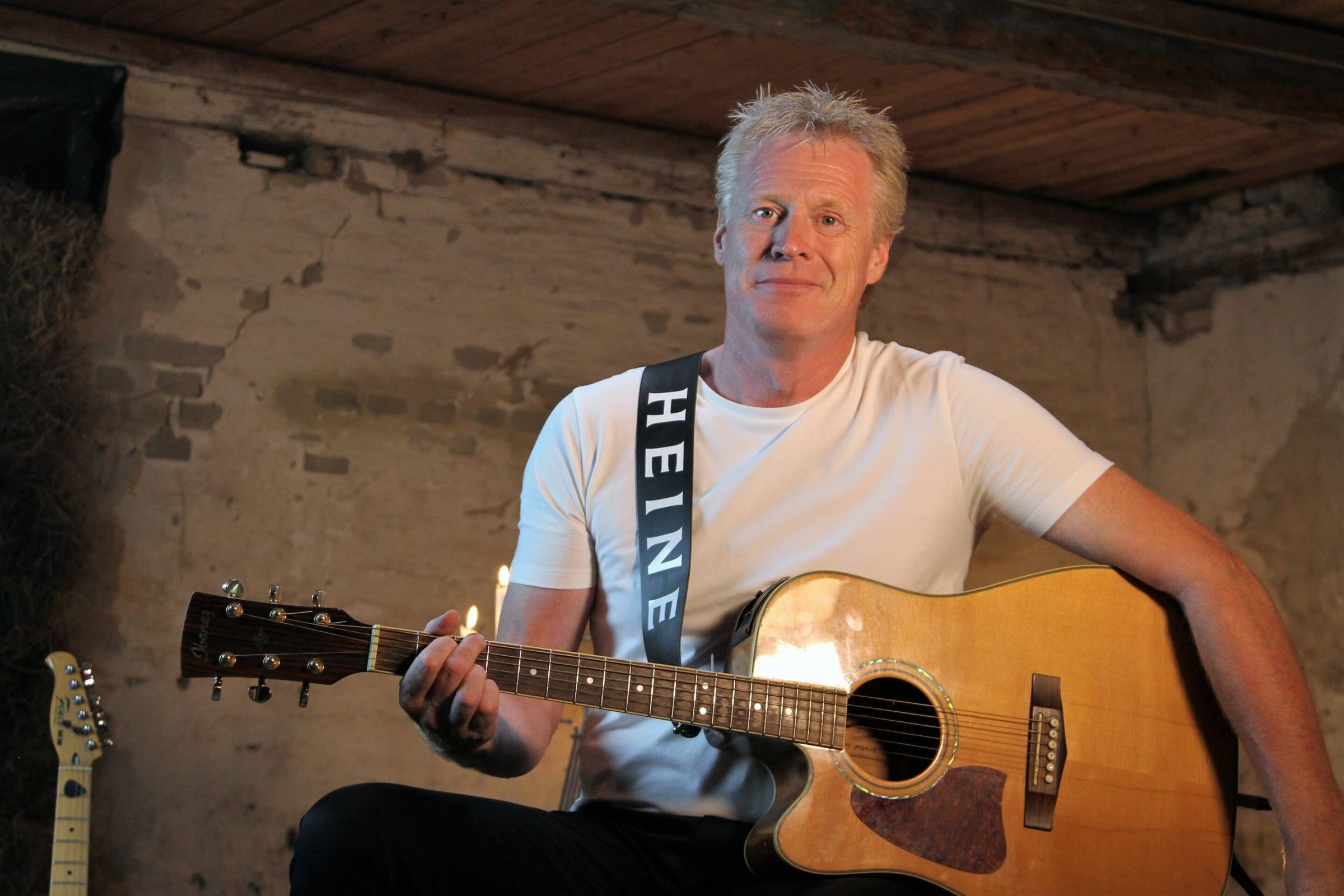 Heine sidder med guitar ved hvid murstensvæg
