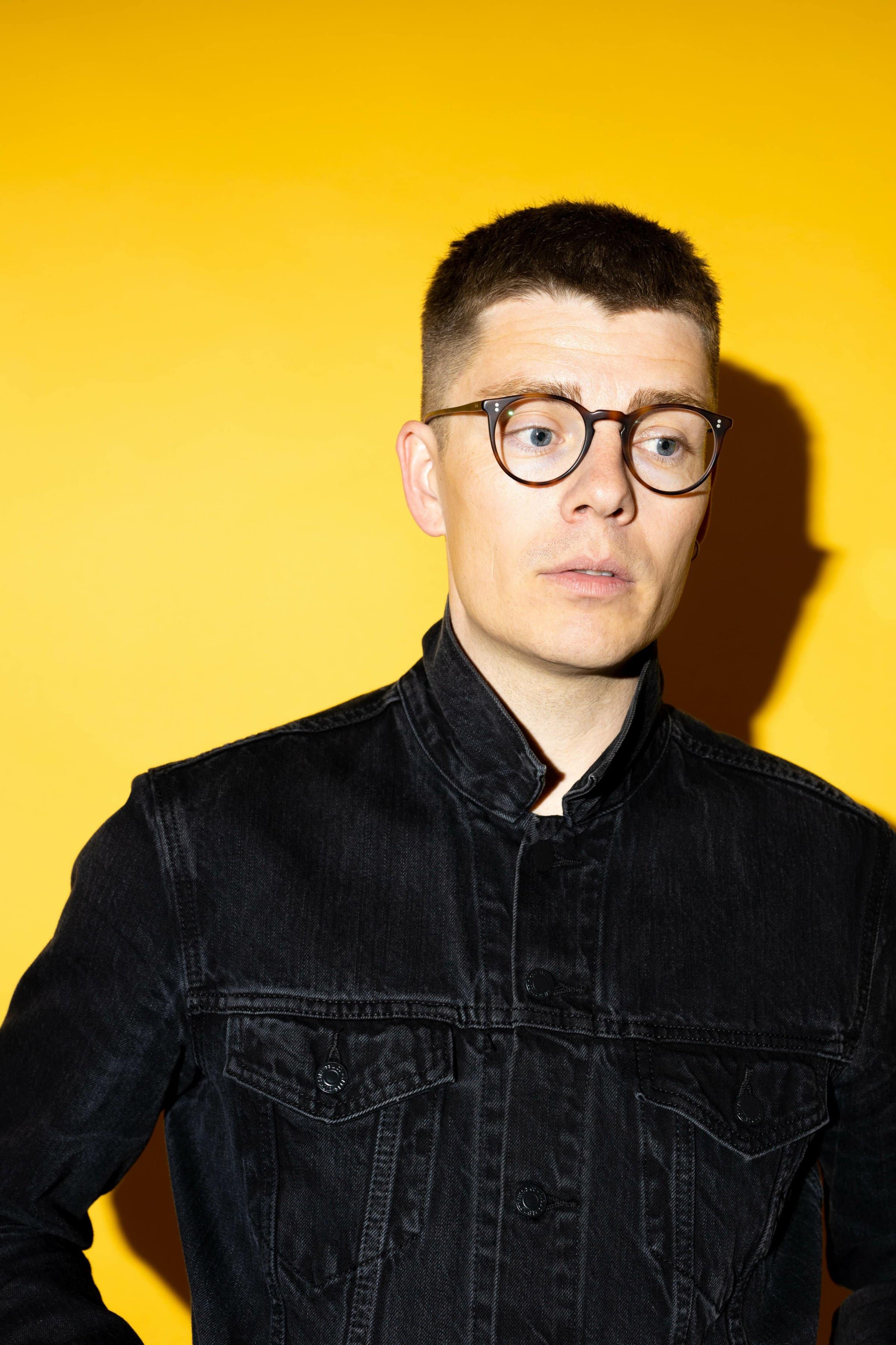 Esben Kronborg med gul baggrund iført sort denimskjorte
