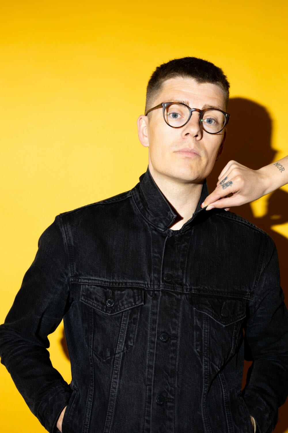 Esben Kronborg med gul baggrund og hånd ved krave