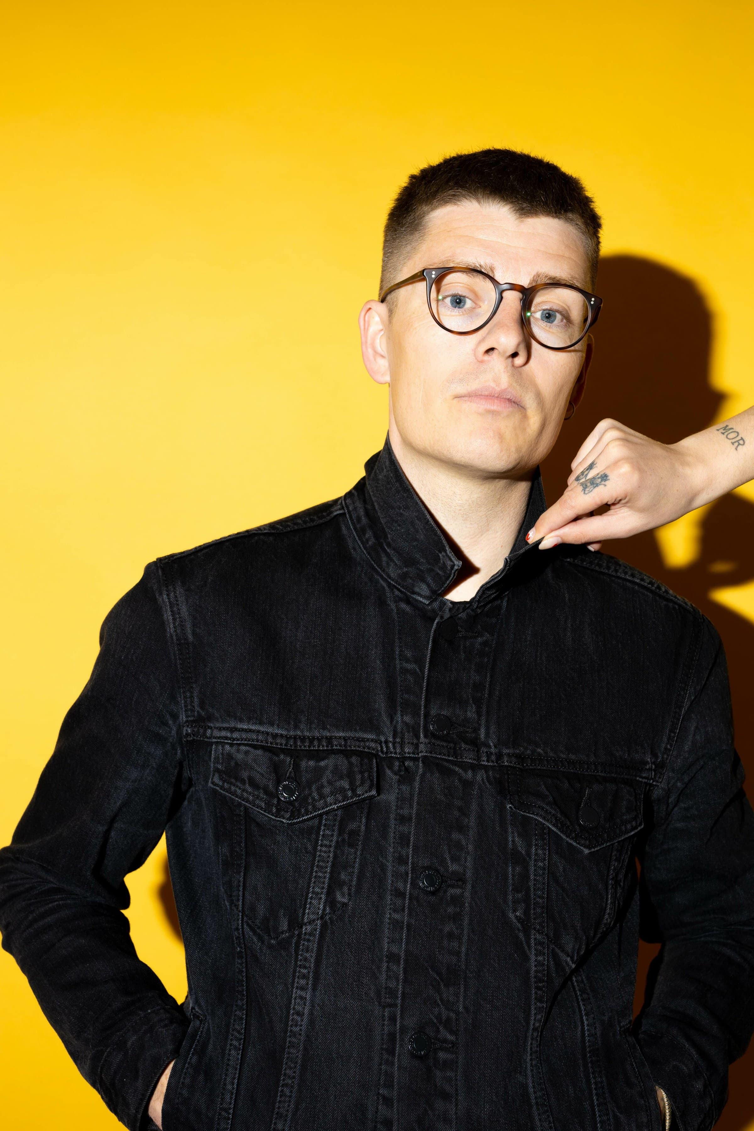 Esben Kronborg med gul baggrund og hånd ved krave